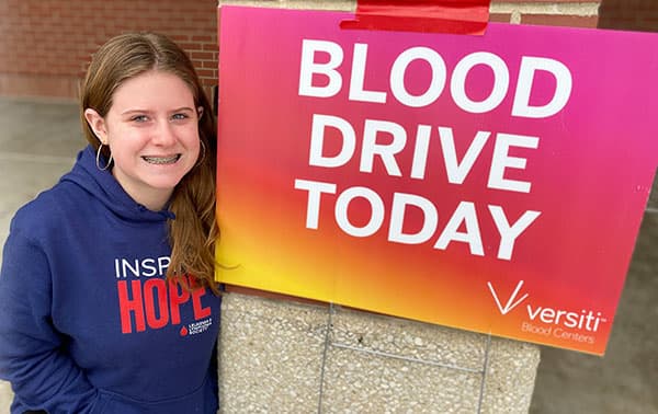 Smiling drive coordinator wtih blood drive sign.