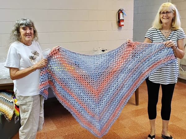 Two volunteers holding a beautiful knitted blanket.