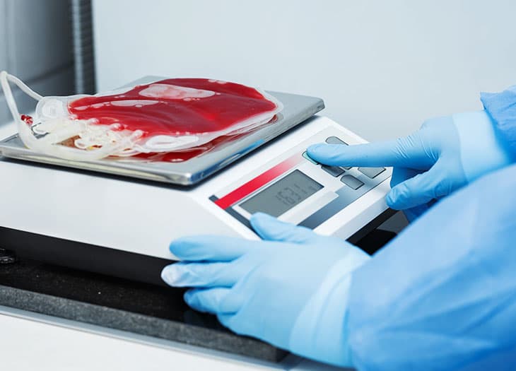 Technician weighing blood unit on scale.