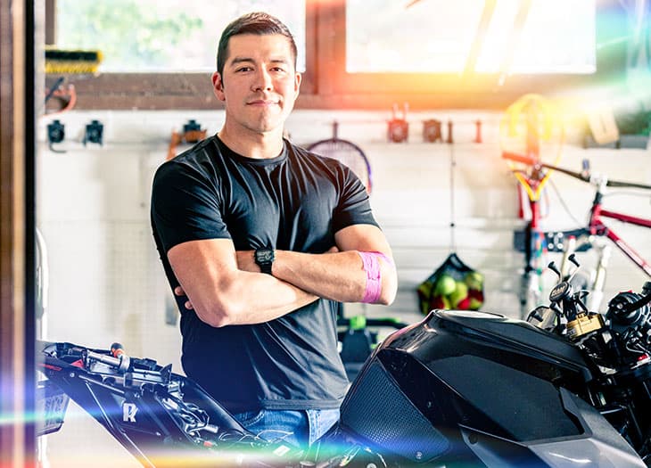Smiling blood donor standing in front of his motorcycle.