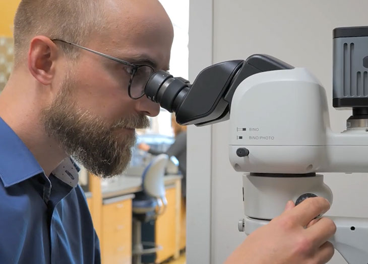 Dr. Wade Sugden pearing into a micrsocope.
