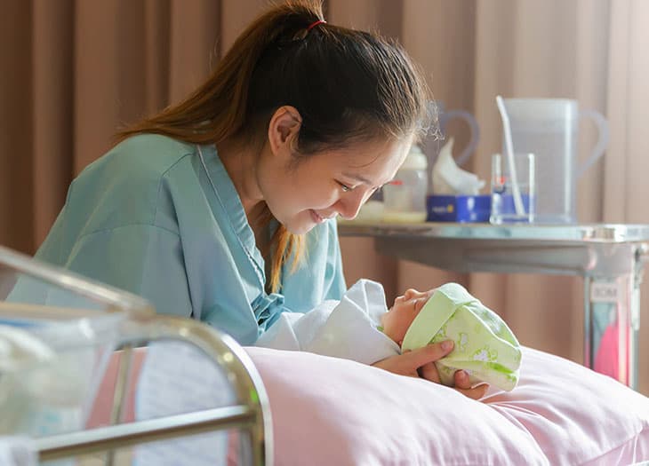 Women smiling holding her newborn baby at the hospital.