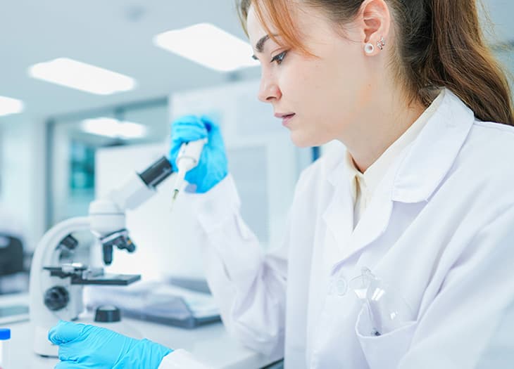 Lab technician holding a pipetting tool next to a microscope.