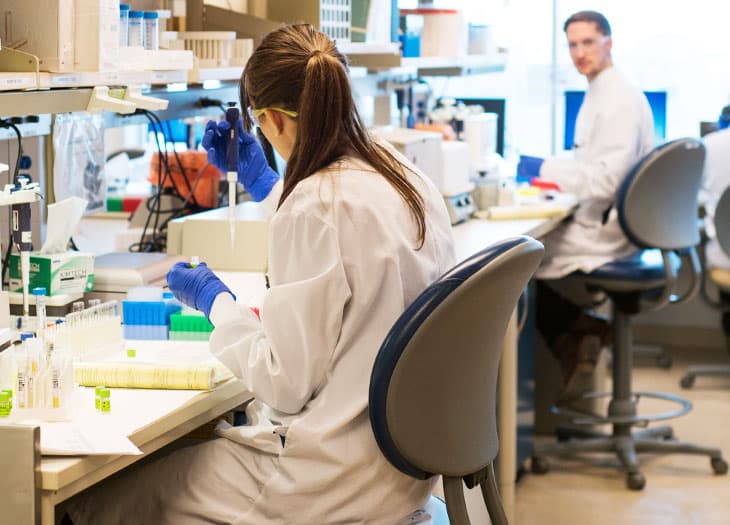 Lab technician pipetting a sample while another technician watches.