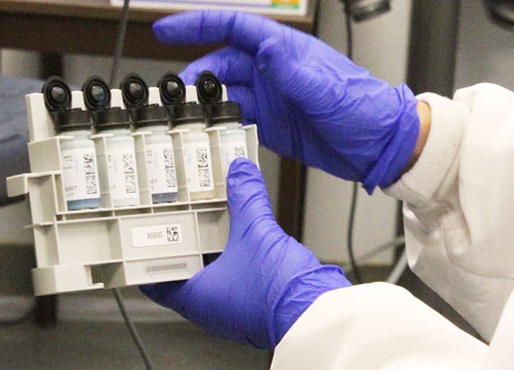 Technician with gloved hands holding 5 donor samples.